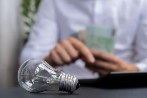Light bulb in focus with a man counting money behind